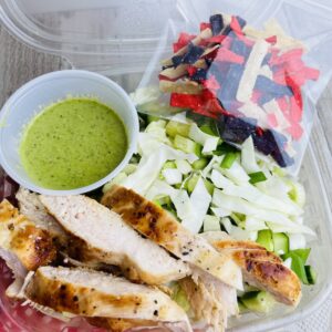 A plastic container filled with salad and chicken.