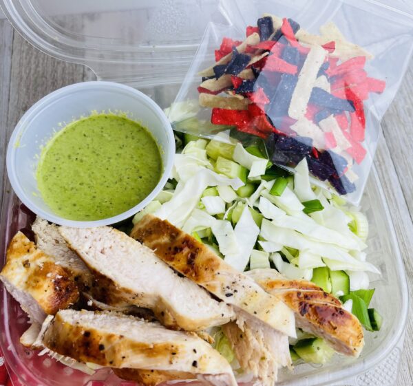 A plastic container filled with salad and chicken.