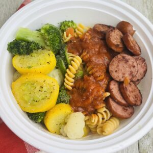 A white bowl filled with pasta, broccoli and sausage.