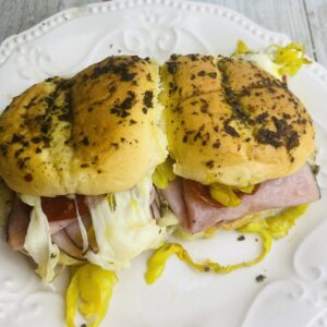 A sandwich on a white plate with mustard and pickles.