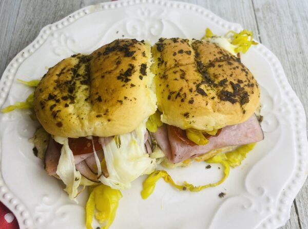 A sandwich on a white plate with mustard and pickles.