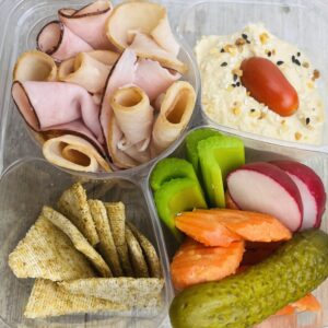 A tray of food with crackers, cheese and vegetables.