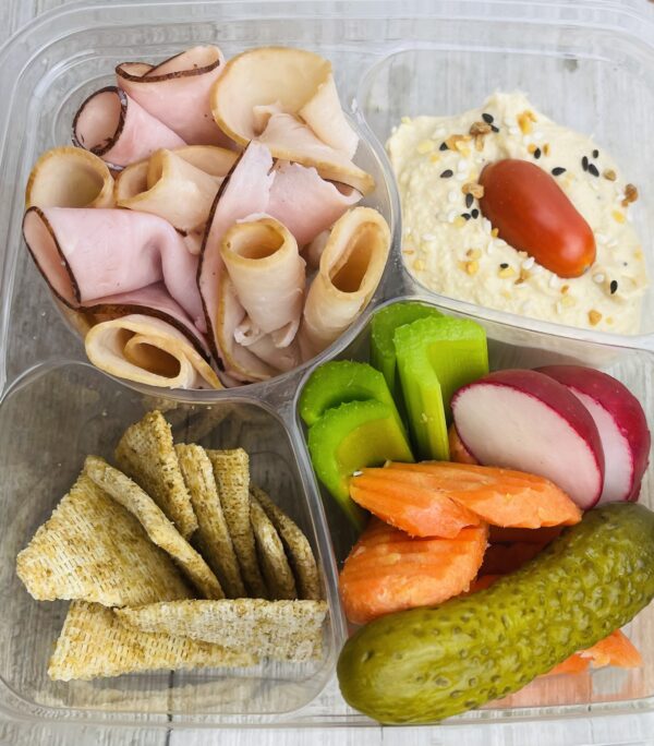 A tray of food with crackers, cheese and vegetables.