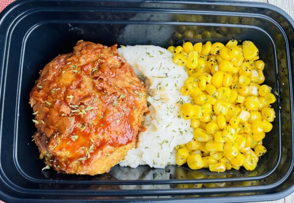 A meal of rice, corn and meat in a container.