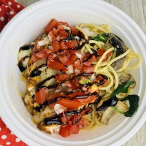 A white bowl of food with tomatoes and zucchini.
